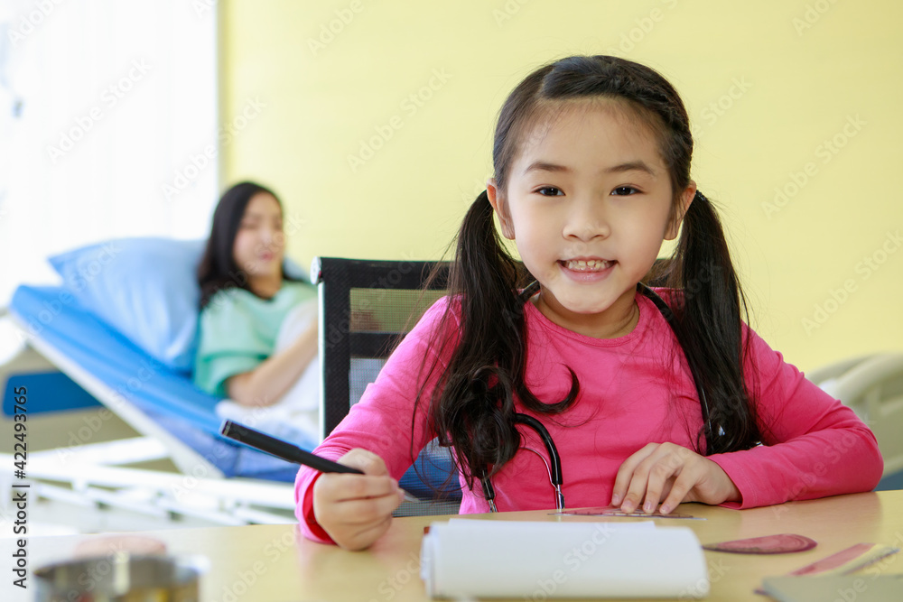 Smiling girl drawing while mother lying on hospital sofa