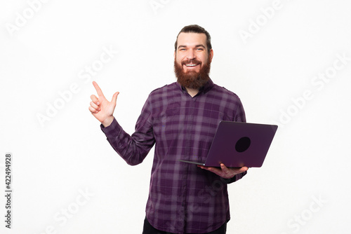 Photo of young handsome man holding laptop and pointing away