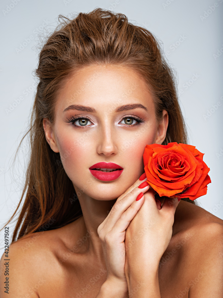 Beautiful young woman with a red flower in hand near face. Portrait of a girl with red rose in hands Beautiful young woman with a red flower in hand near face. Portrait of a girl with red rose in hands