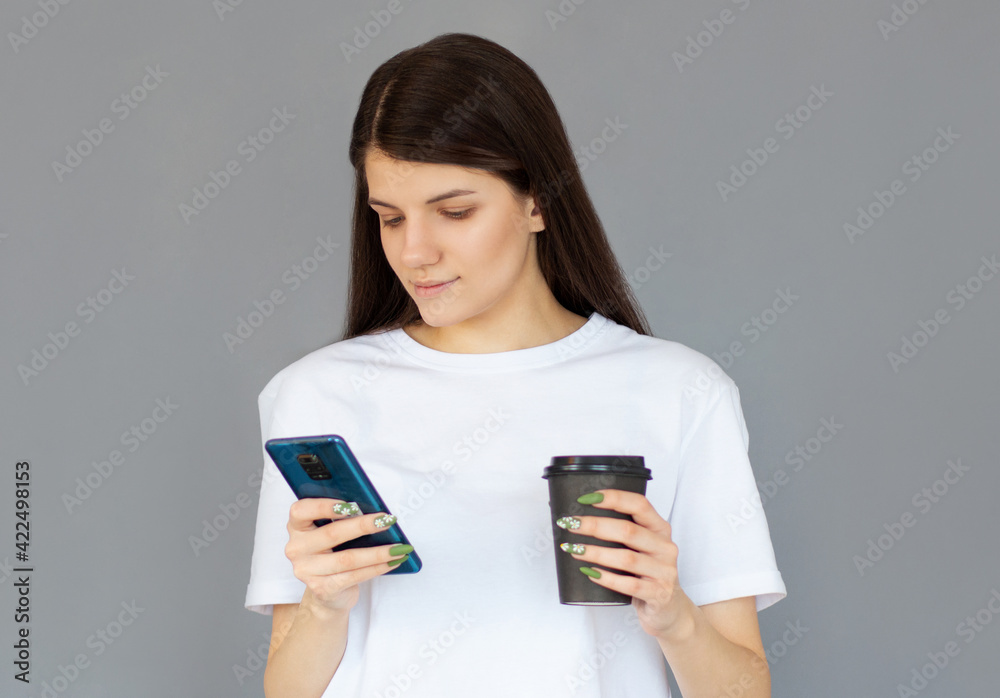 Portrait of a satisfied young business woman using mobile phone while holding cup of coffee to go isolated over gray background Portrait of a satisfied young business woman using mobile phone while holding cup of coffee to go isolated over gray background