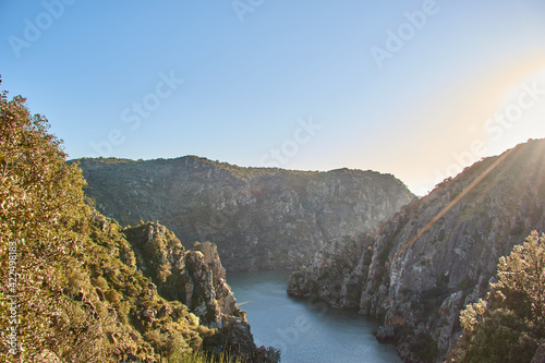Three rocky mountains with cliffs and a river at sunset.
