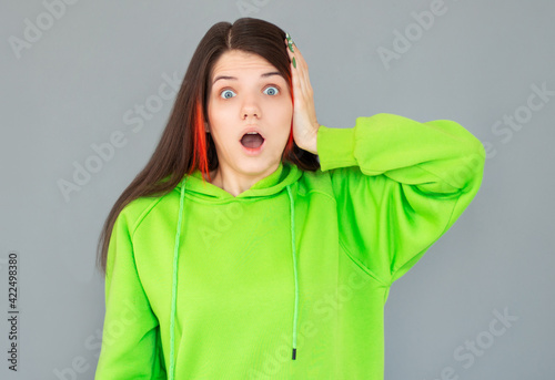 Shocked amazed young woman with hand on head standing and shouting over gray background © Яна Солодкая
