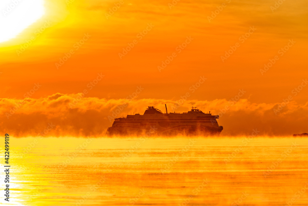 Fog over the Baltic sea during a strong frost in the sunset. The ferry ship silhouette on the horizon.