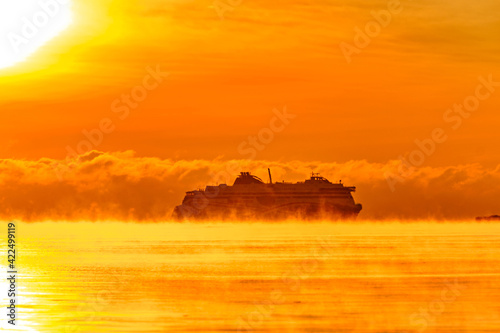 Obraz na płótnie Fog over the Baltic sea during a strong frost in the sunset. The ferry ship silhouette on the horizon. w salonie