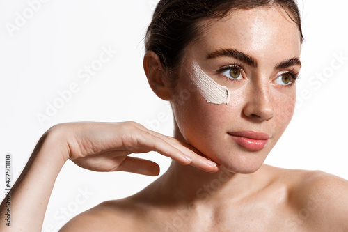 Beauty woman applying face cream on clean fresh skin, detoxifying effect, moisturize and hydrate facial with scrub, nourishing effect of mask, looking aside, white background