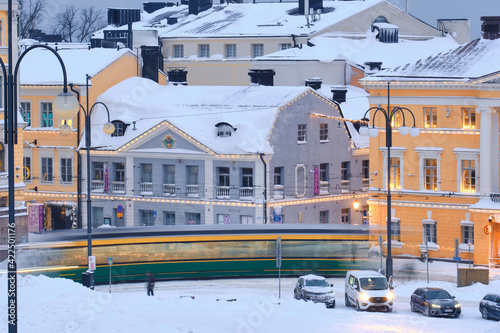 Obraz na płótnie Helsinki, Finland - January 13, 2021: The tram is moving on the Senate Square during the strong snowstorm. The blue building is Helsinki City Museum w salonie