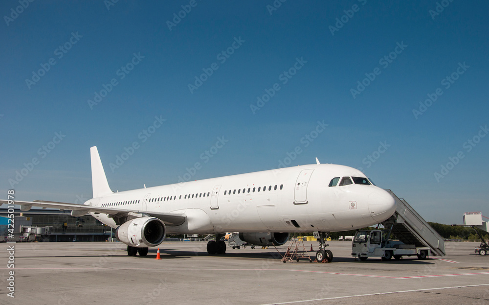 A commercial white airplane parked at the airport in sunny day. Preparation for next flight. Plane against the background of the airport. Aircraft maintenance. Space for text.