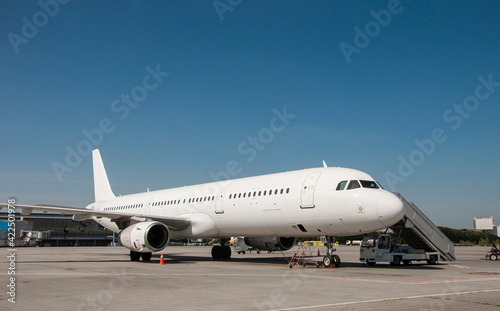 A commercial white airplane parked at the airport in sunny day. Preparation for next flight. Plane against the background of the airport. Aircraft maintenance. Space for text. © Ivan