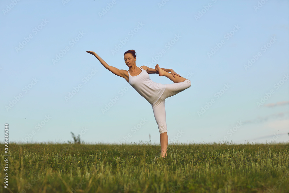 Slim yoga instructor doing Standing Bow pose on green summer meadow under clear blue sky Slim yoga instructor doing Standing Bow pose on green summer meadow under clear blue sky