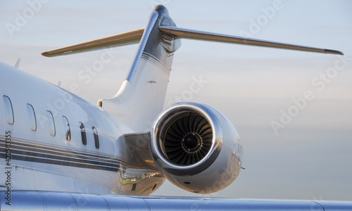 Business travel concept. Jet engine on parked luxury private jet. Rear detail with engine, tail-plane and windows of business-jet aircraft. Space for text.
