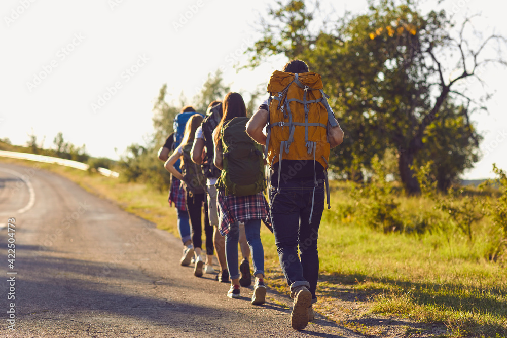 Obraz premium Group of young hikers walk in a row along the road with backpacks on their shoulders.
