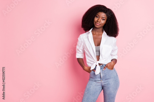 Portrait of attractive content girl holding hands in pockets posing copy space isolated over pink pastel color background