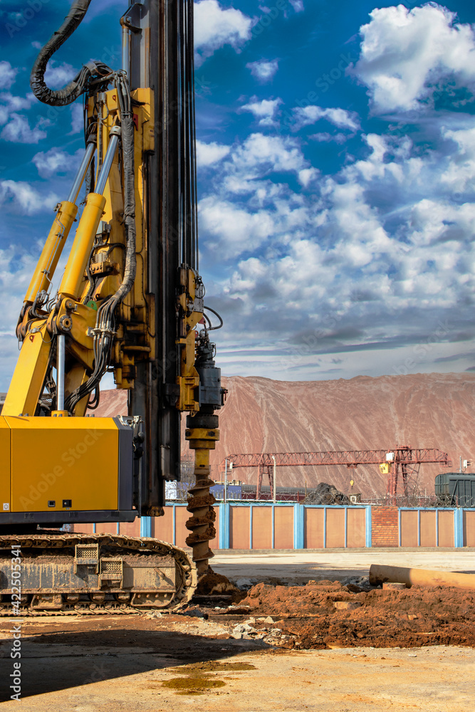 Hydraulic drilling rig against the blue cloudy sky. Vertical image. Installation of bored piles by drilling. Foundations and foundations. Drilling in the ground. Hydraulic drilling rig against the blue cloudy sky. Vertical image. Installation of bored piles by drilling. Foundations and foundations. Drilling in the ground.