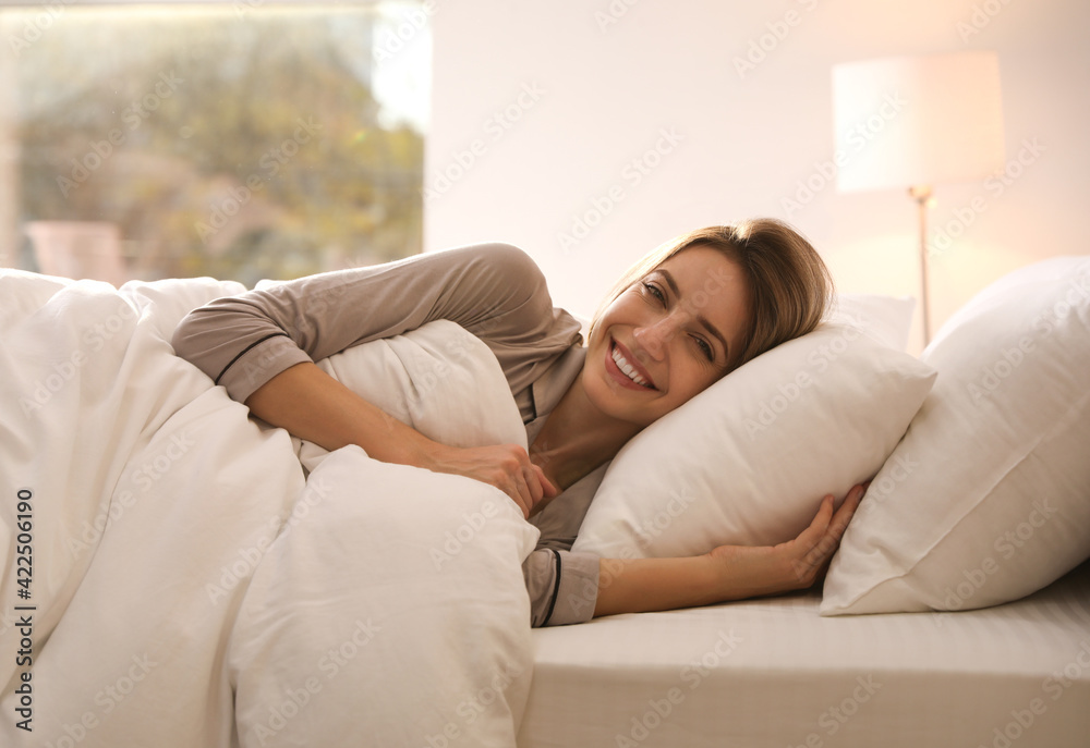 Cheerful woman under warm white blanket lying in bed indoors Cheerful woman under warm white blanket lying in bed indoors