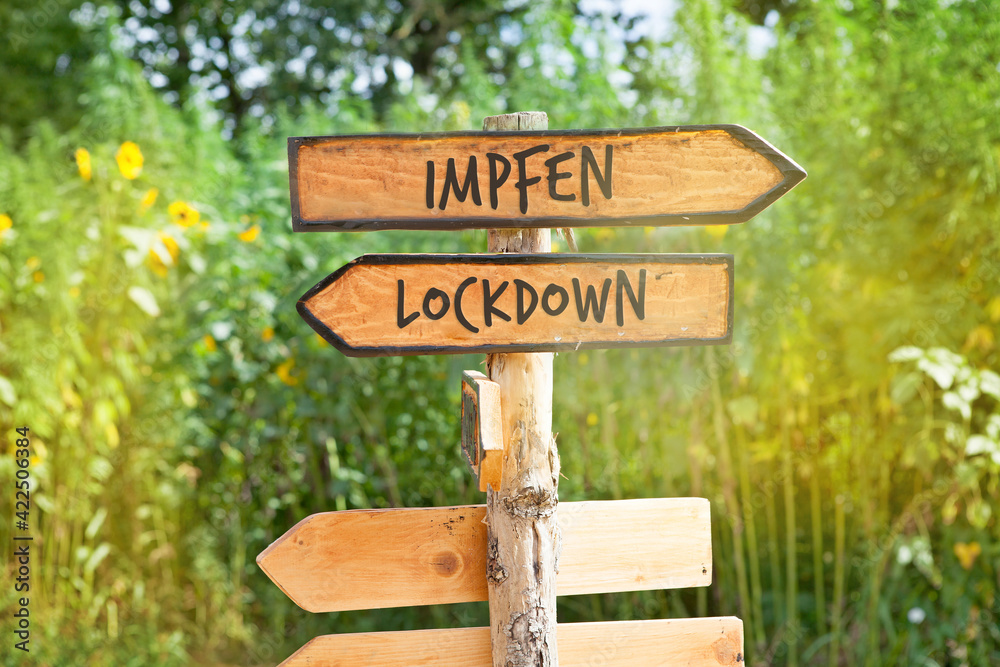 Wooden direction sign with the German word impfen (vaccinate) and Lockdown