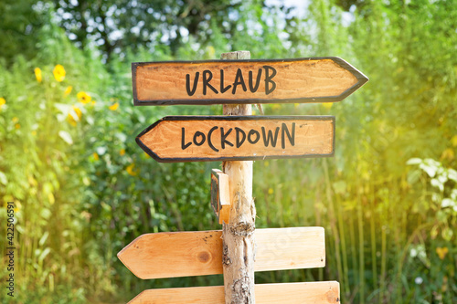 Wooden direction sign with the German word Urlaub (vacation) and Lockdown