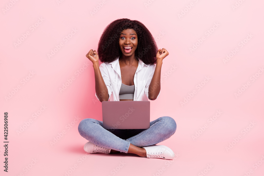 Portrait of attractive cheerful girl sitting in lotus position using laptop rejoicing isolated over pink pastel color background Portrait of attractive cheerful girl sitting in lotus position using laptop rejoicing isolated over pink pastel color background