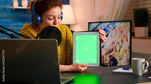 Influencer holding tablet with green screen and speaking into microphone during podcast in home studio. On-air production internet broadcast host streaming live content using chroma key mockup display