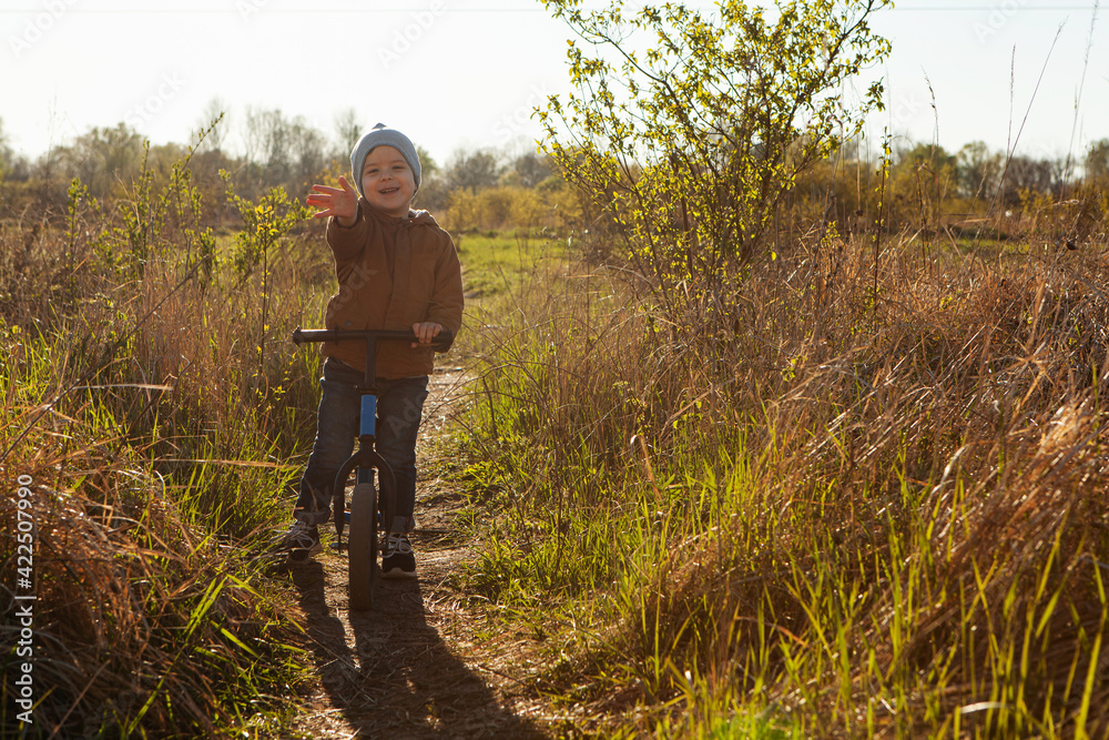 A boy rides a balance bike in a clearing. Spring mood. Sun