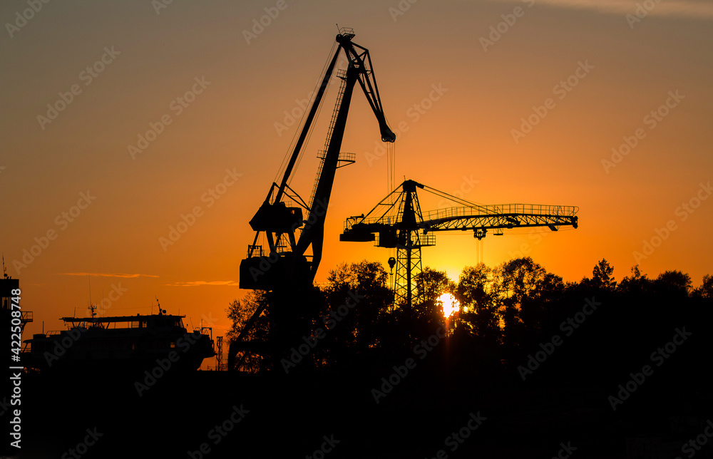 River boat and floating river cranes on the river bank at sunset River boat and floating river cranes on the river bank at sunset