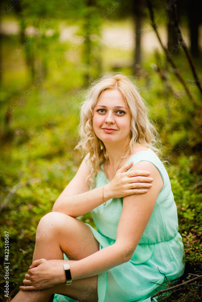Young beautiful blonde in a light green dress posing in the woods in summer, selective focus Young beautiful blonde in a light green dress posing in the woods in summer, selective focus