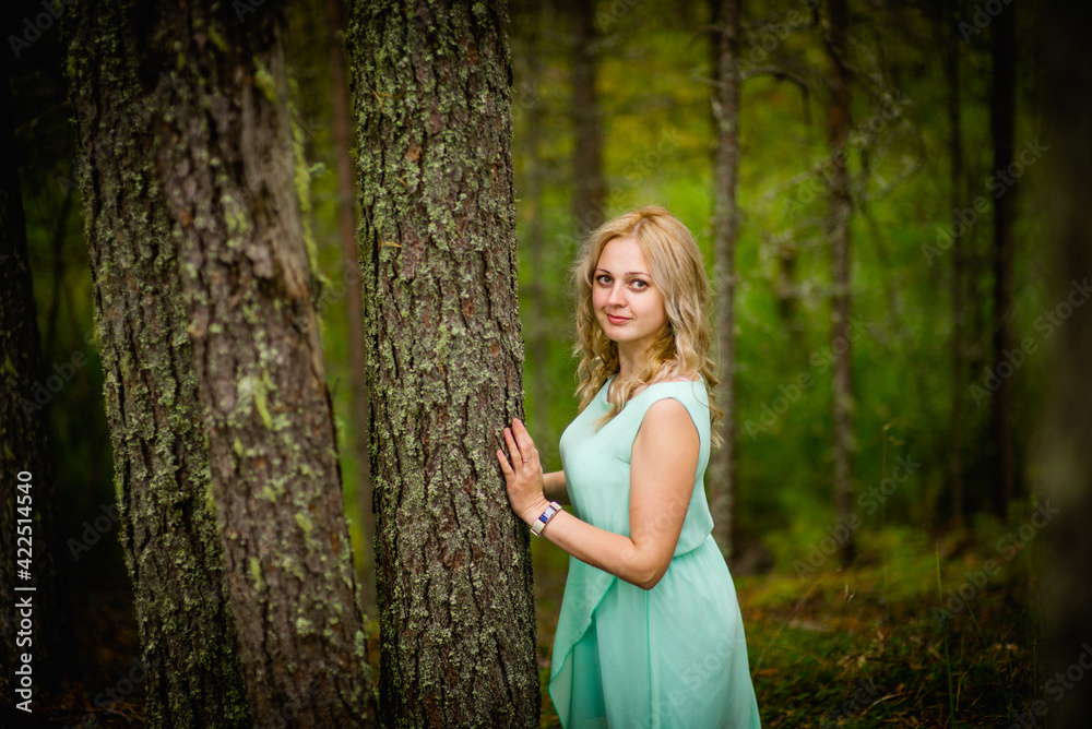 Young beautiful blonde in a light green dress posing in the woods in summer, selective focus Young beautiful blonde in a light green dress posing in the woods in summer, selective focus