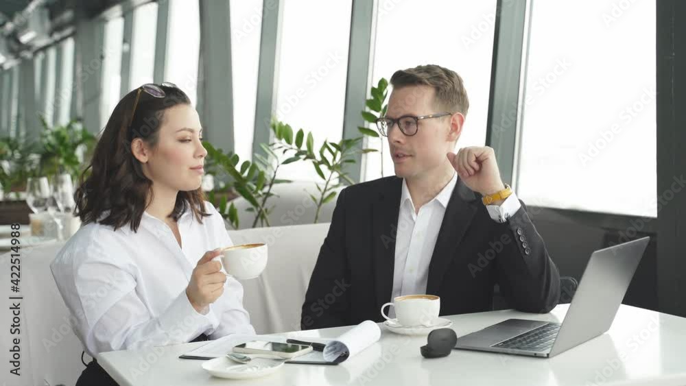 Business partners talking at meeting in restaurant, man and woman sit with laptop at table, co-working, wearing formal clothes, with laptop. Business partners talking at meeting in restaurant, man and woman sit with laptop at table, co-working, wearing formal clothes, with laptop.
