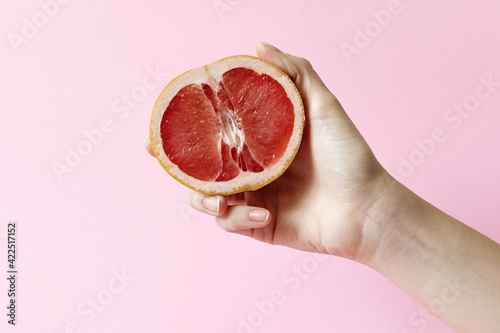 Female hands holding half grapefruit on pink background, female masturbation concept