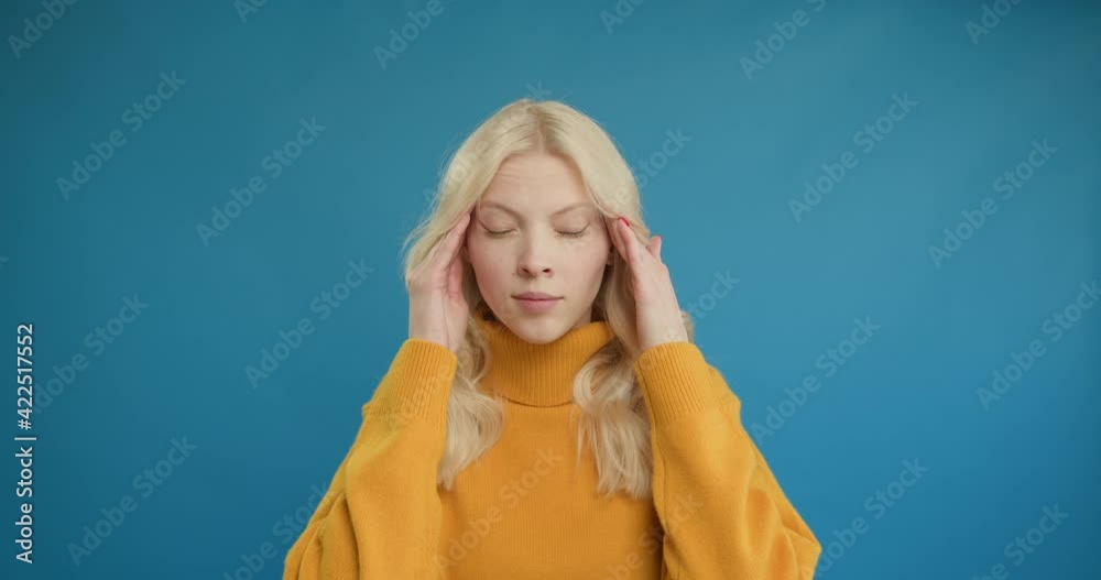 Closeup exhausted woman with migraine posing at camera. Portrait of tired girl having headache on blue background. Stressed woman touching head with hands in studio Closeup exhausted woman with migraine posing at camera. Portrait of tired girl having headache on blue background. Stressed woman touching head with hands in studio