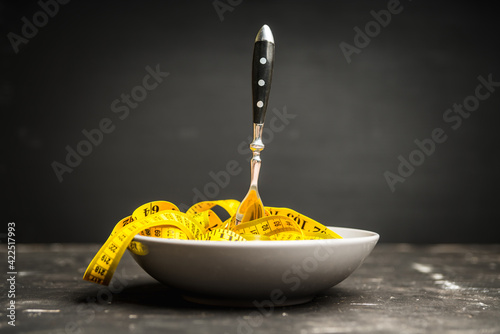 Yellow measuring tape in bowl like spaghetti with fork. Concept of diet. Selective focus. 