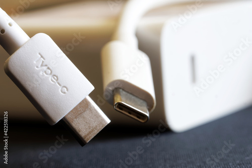 Two white usb type-c connectors on a dark background next to a white power supply and fast charger. The concept of modern technology and data transmission. Close-up. Macro