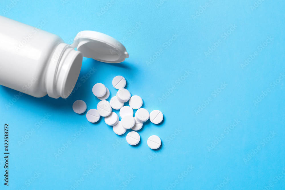 Pills and bottle on light blue background, above view. Space for text