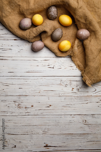 Vertical photo, Easter colored eggs yellow and gray on a rustic-style fabric on a light wooden background with space for text. Easter. Celebration. High quality photo