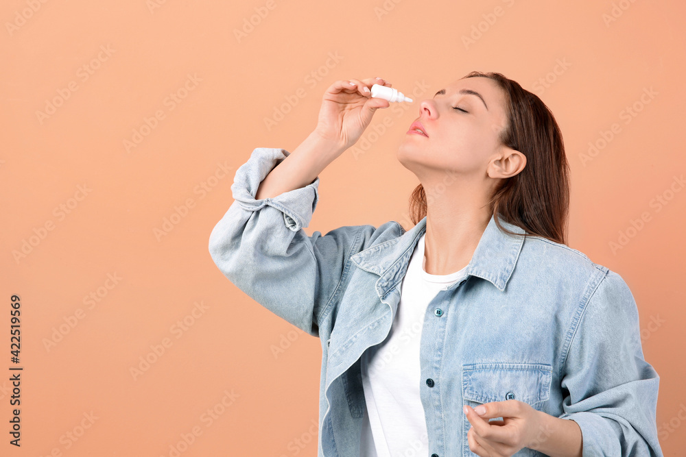 Woman using nasal spray on peach background, space for text Woman using nasal spray on peach background, space for text
