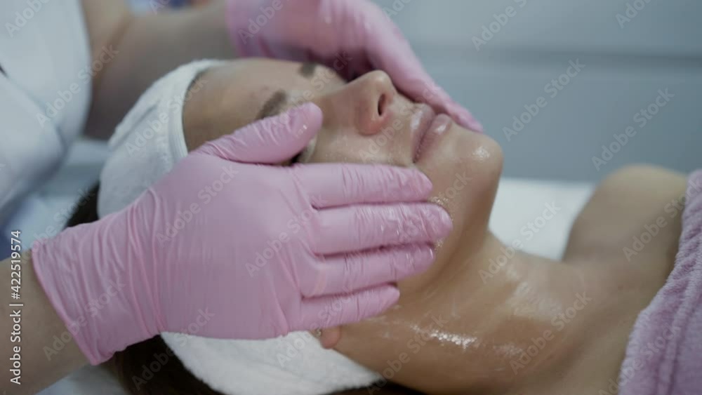 Close view of beautician's hands massage female face with cleansing liquid