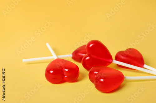 Sweet heart shaped lollipops on yellow background, closeup view with space for text. Valentine's day celebration