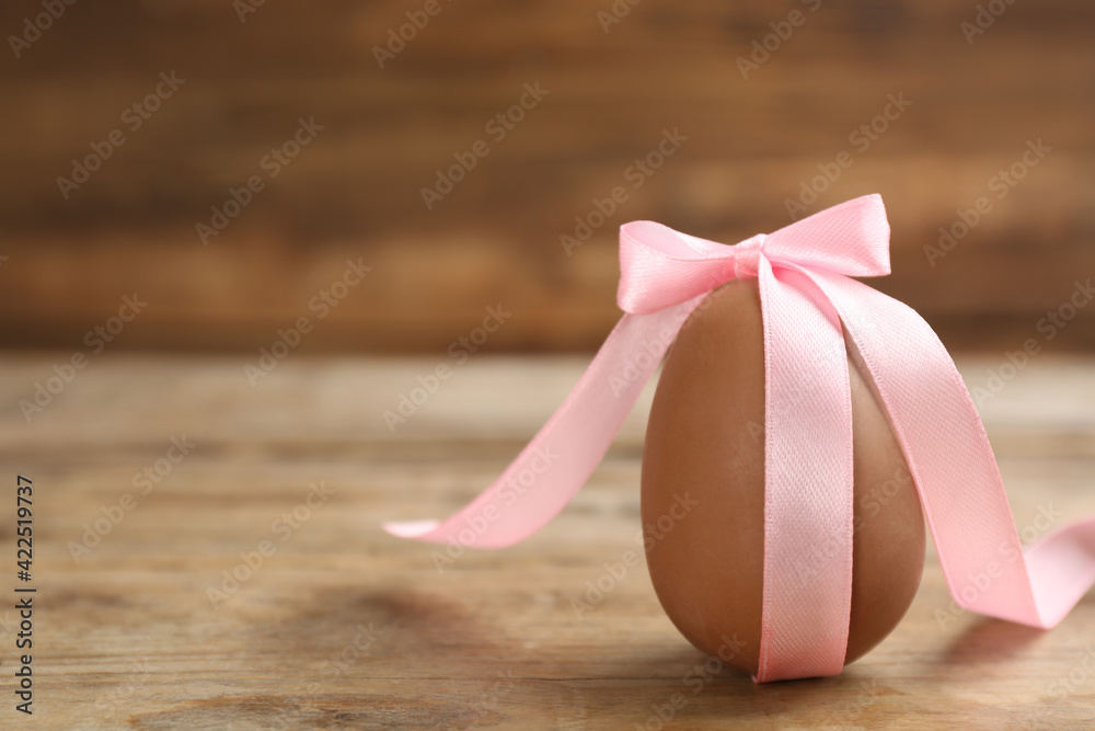 Sweet chocolate egg with pink bow on wooden table. Space for text Sweet chocolate egg with pink bow on wooden table. Space for text
