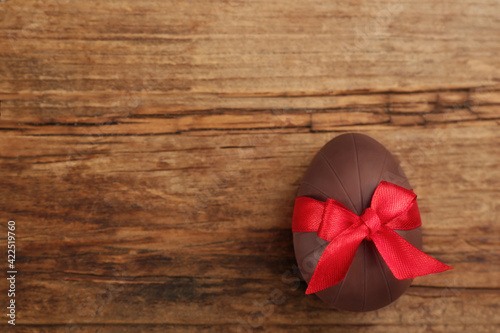 Sweet chocolate egg with red bow on wooden table, top view. Space for text