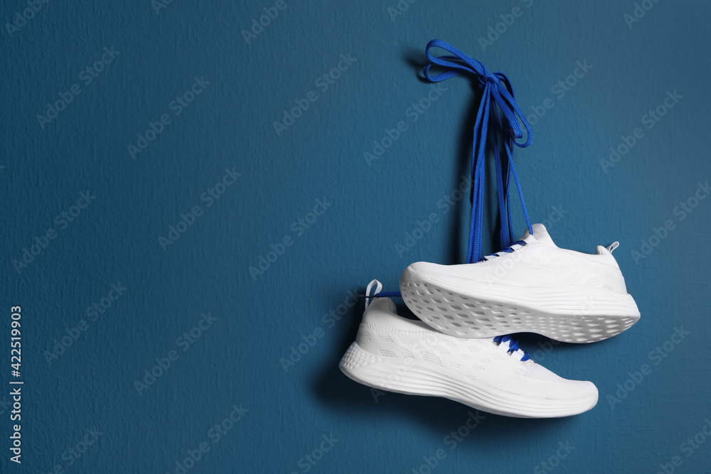 Pair of stylish shoes with laces hanging on blue wall, space for text - obrazy, fototapety, plakaty 