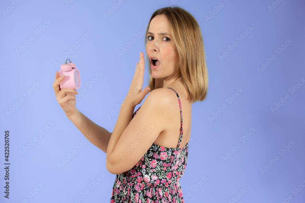 Portrait of cheerful young surprised woman holding alarm clock isolated over purple background Portrait of cheerful young surprised woman holding alarm clock isolated over purple background