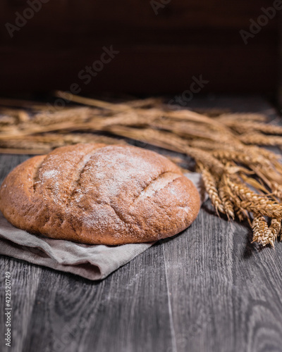 craft bread and ears of wheat on a dark wooden background, soft selective focus, vertical