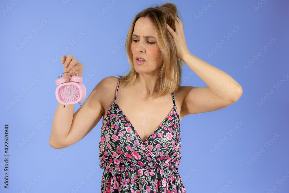 Portrait of cheerful young doubtful woman holding alarm clock isolated over purple background Portrait of cheerful young doubtful woman holding alarm clock isolated over purple background