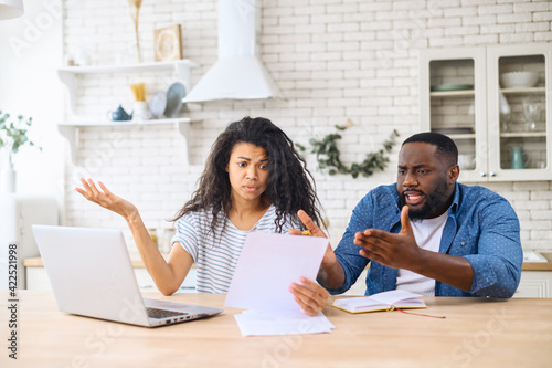 Anxious mixed race couple looking through domestic bills, reading papers at home, worried biracial wife and african husband calculating family budget,not enough money on bank account to repay the loan