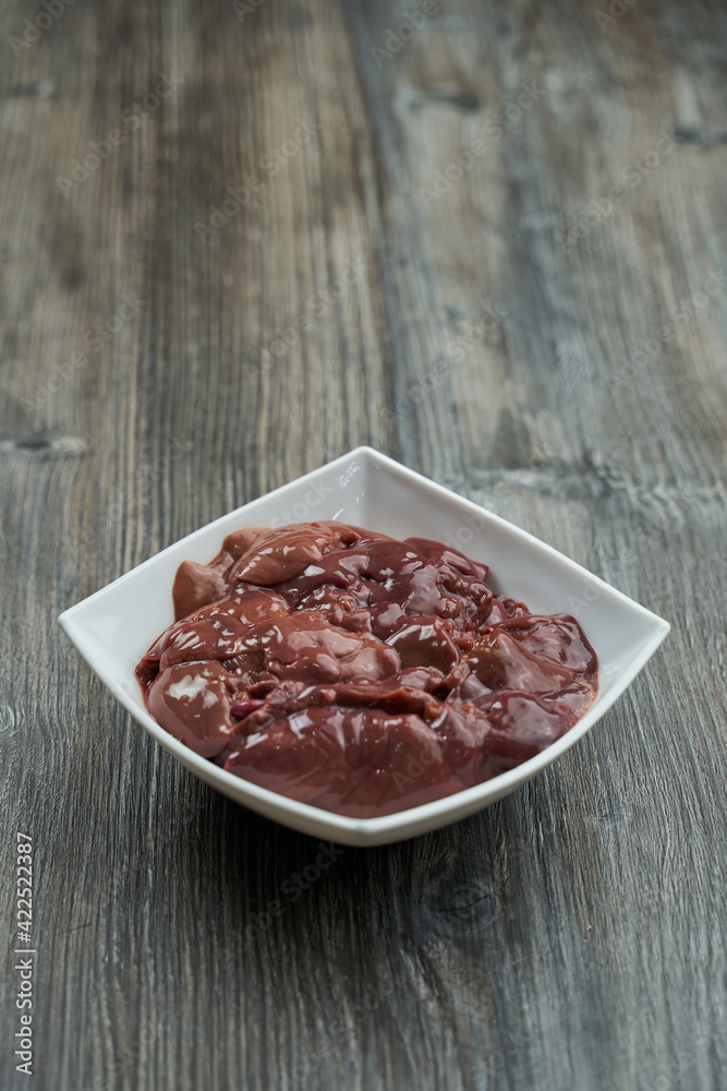 raw chicken liver in a white plate on a gray wooden table.