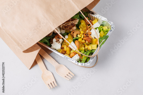 Diet fresh meat salad with a lot of greens, grilled chicken, feta on white background. Healthy low-calorie lunch in foil container to go, from cafe to take away. Concept restaurant delivery