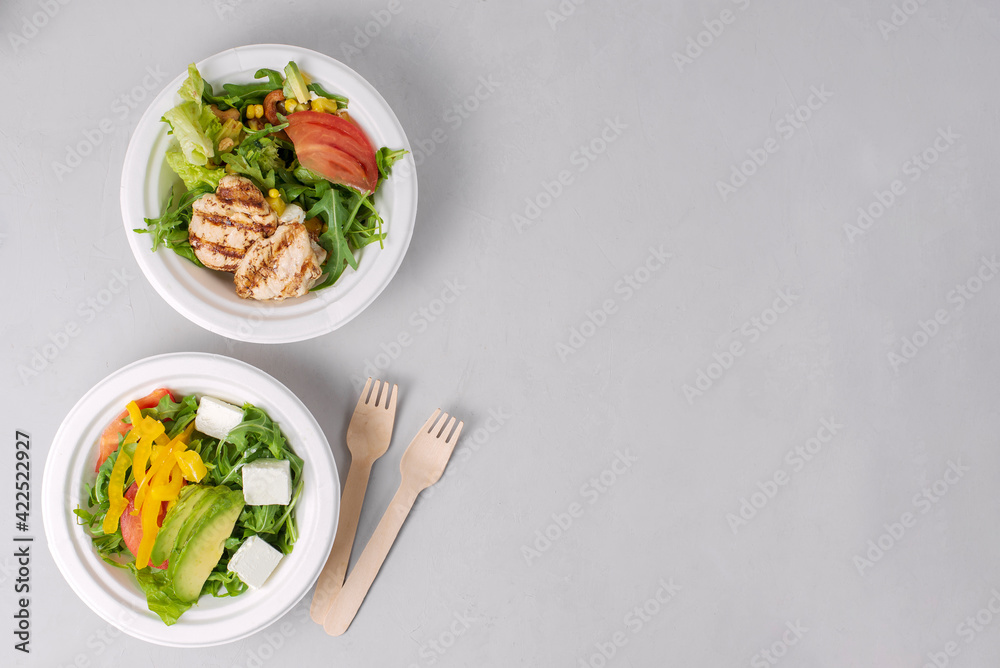 Two diet light salads with chicken, tomatoes, avocado, greens, white background. Healthy lunch. Take away food in eco paper plates. Concept restaurant delivery, environment protection. Copy space Two diet light salads with chicken, tomatoes, avocado, greens, white background. Healthy lunch. Take away food in eco paper plates. Concept restaurant delivery, environment protection. Copy space