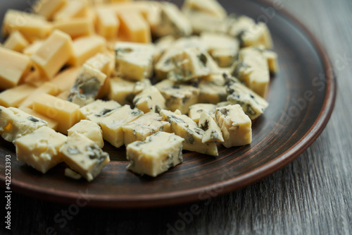 a brown plate on which two types of cheese, in the foreground blue dor blue cheese, cut into cubes. selective focus