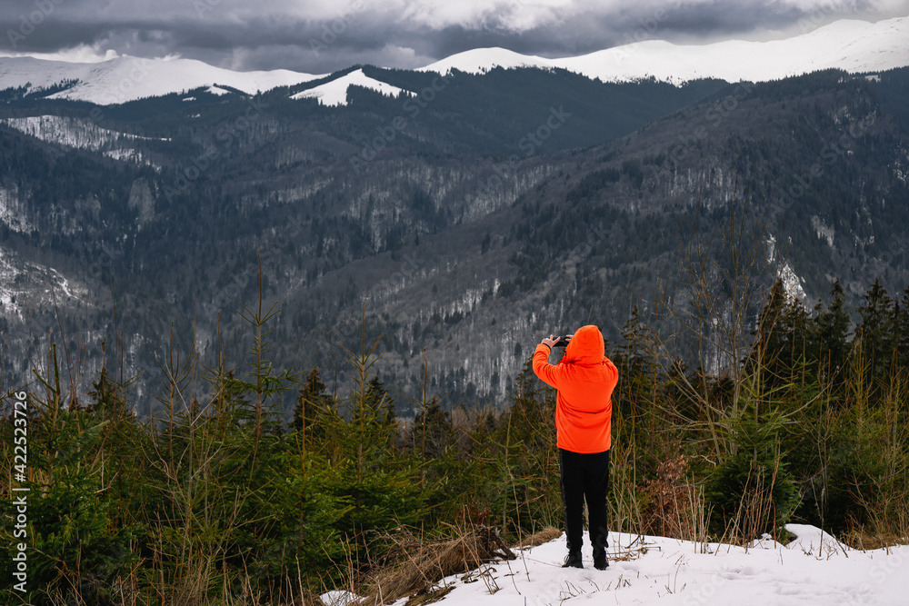 person in orange jacket taking photos of winter snowy mountain