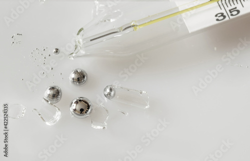Broken glass mercury thermometer on light grey surface. Mercury drops with glass fragments. Mercury vapor poisoning.