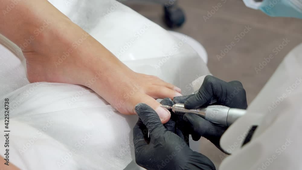 Close-up shot of hands in gloves doing a pedicure procedure with a special device in modern spa salon. Hardware medical pedicure with nail file drill apparatus.